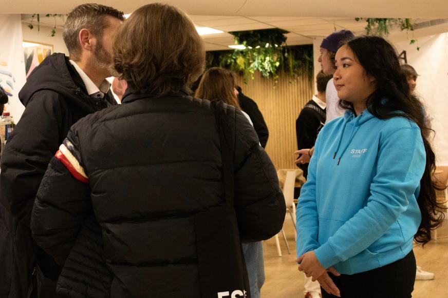 Femme brune étudiante avec un pull a capuche bleu discute avec deux hommes